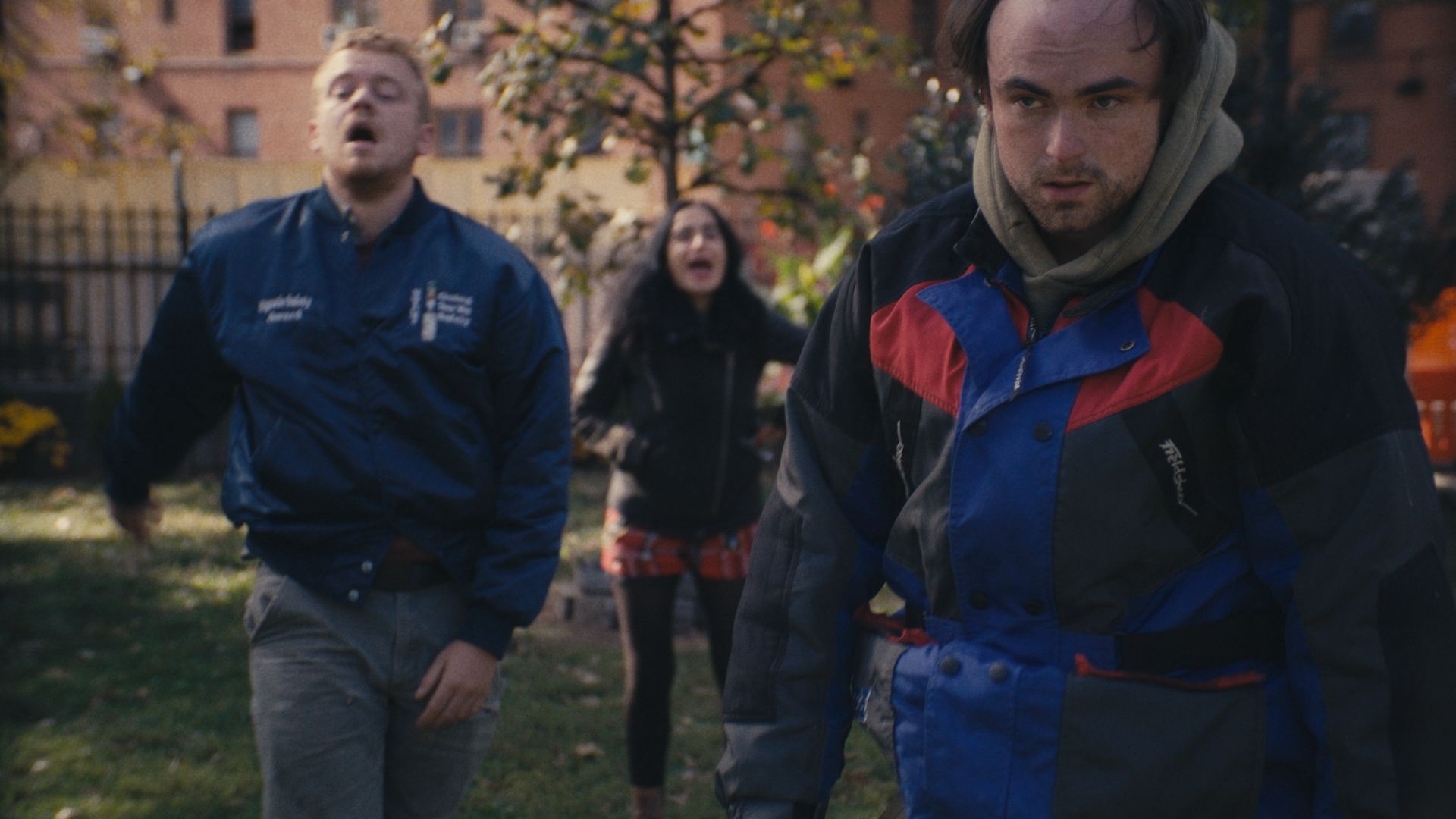 Three friends cross a small city park in autumn; the two behind are shouting.