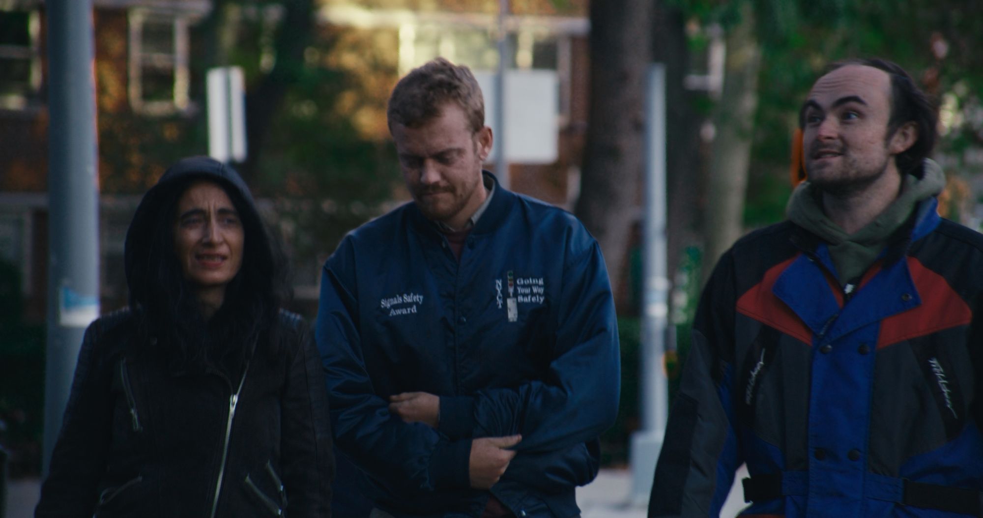 The three friends walk down a leafy street at dusk.