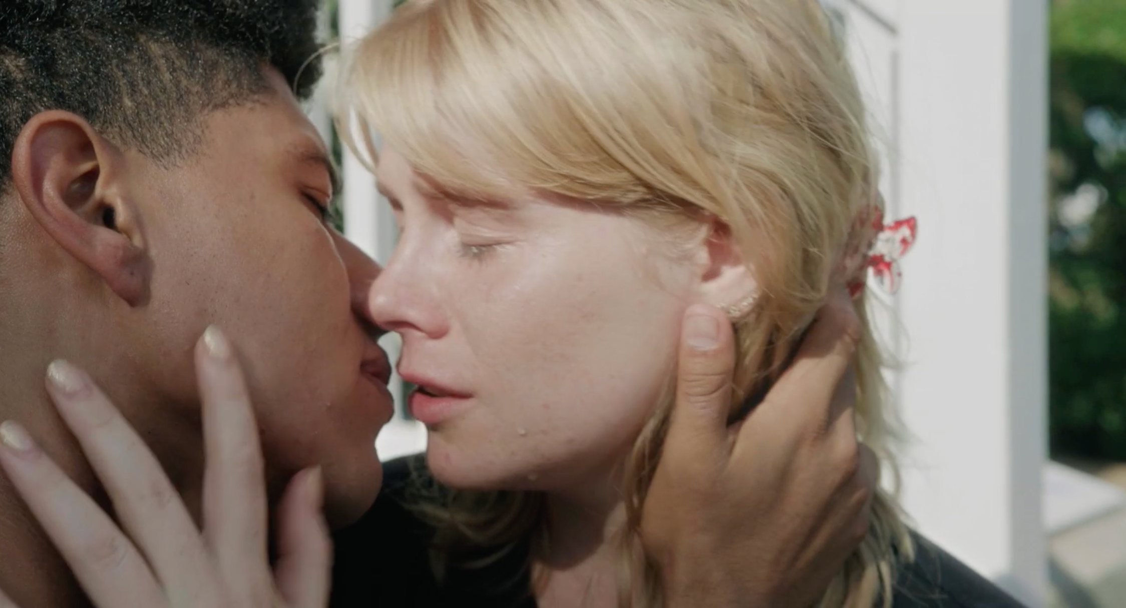 A tearful kiss in bright sunlight, her hands on his face.