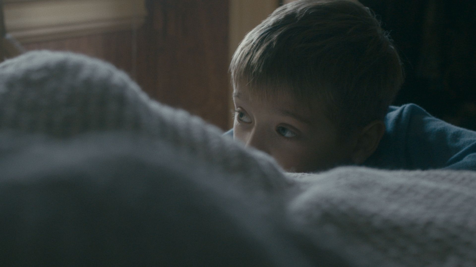 A boy peers over the edge of a blanket.
