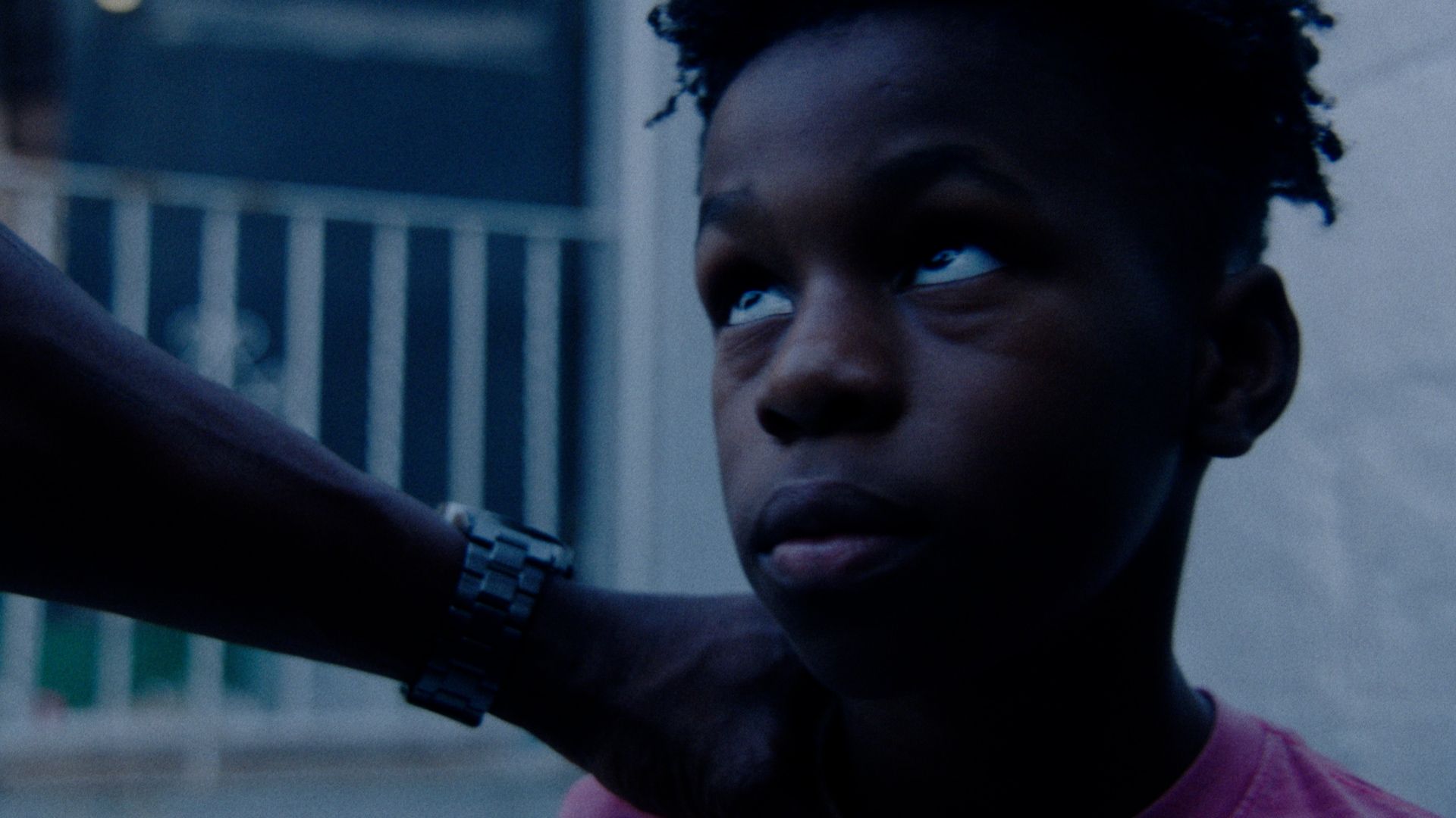 A boy looks up, a man's arm resting on his shoulder.
